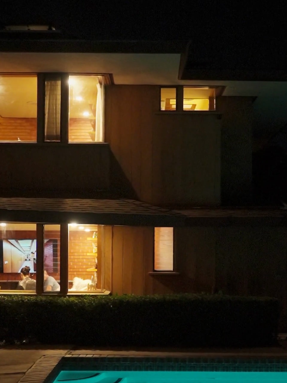 La maison du crépuscule · Tombée de la nuit : les lumières s'allument, les invités sont encore à l'intérieur, la piscine rayonne